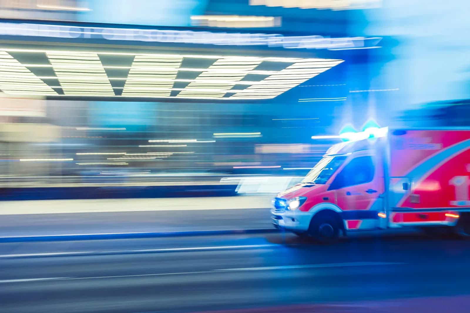 Mavi tepe lambaları yanan bir ambulans, hareket bulanıklığıyla cadde boyunca ilerliyor.
