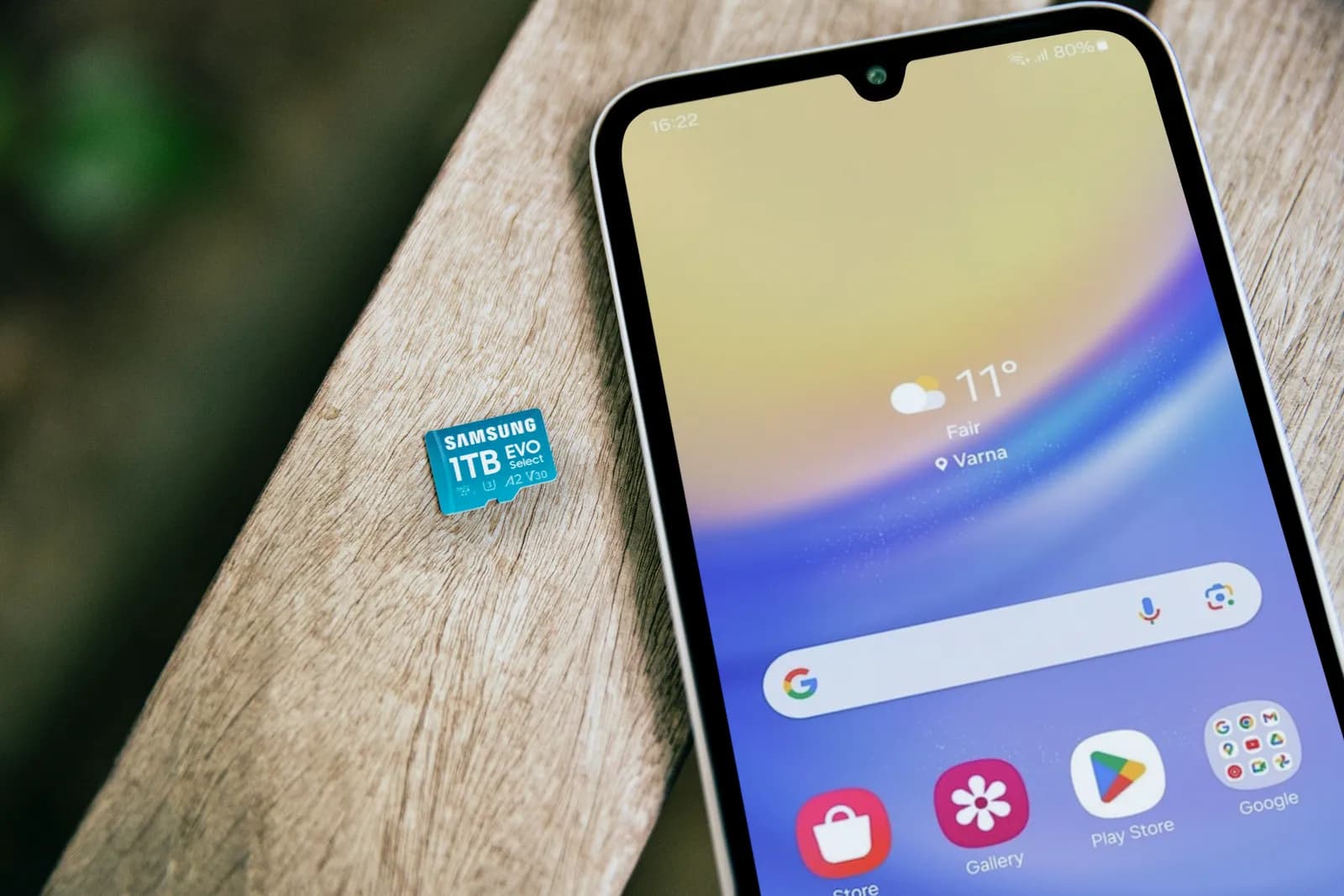 Ahşap bir masada ekranı açık akıllı telefon; yanında tırnak büyüklüğünde bir hafıza kartı duruyor.